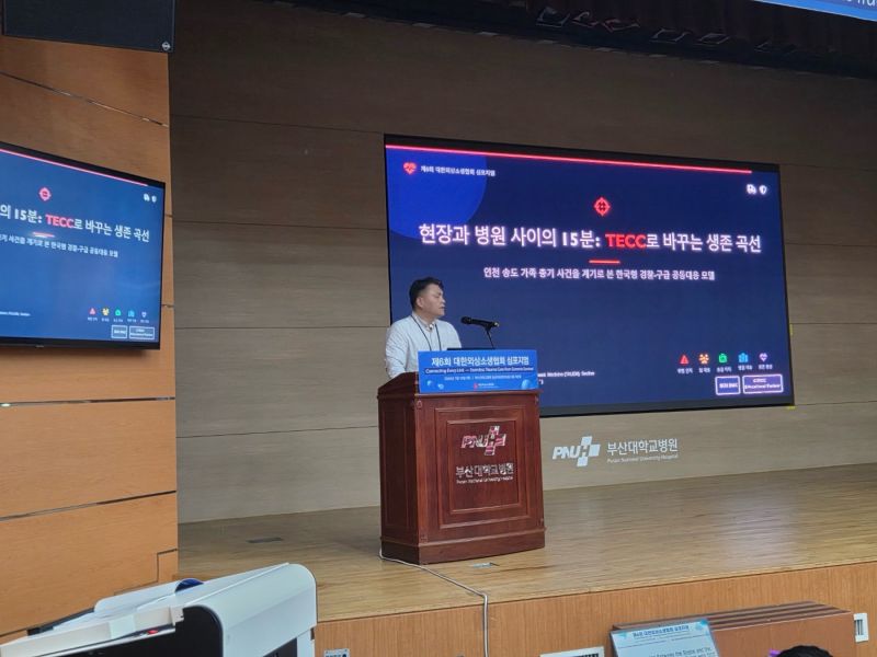 연단에서 TECC 강연을 진행하는 장면. 화면에 현장과 병원 사이의 15분이라는 강연 제목이 보임.